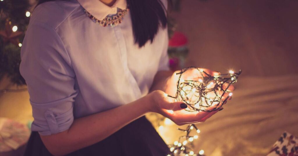 Woman kneeling in low lit room with lit Christmas lights cupped in her hands