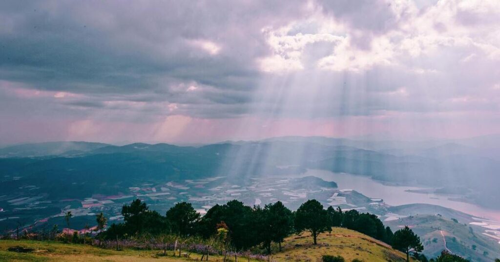 Sunbeams coming through cloud cover onto a hilly landscape.