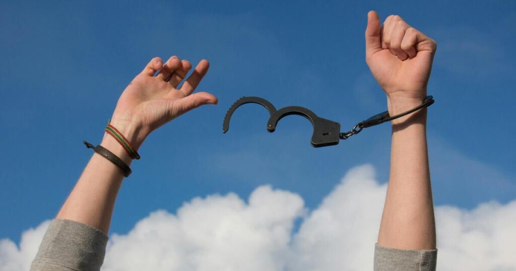 Arms raised in front of blue sky backdrop, being released from handcuffs.