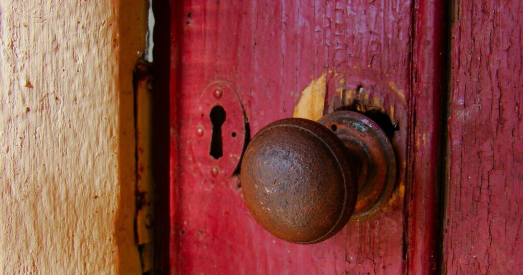 Closeup of red-painted door with keyhole and rustic doorknob.