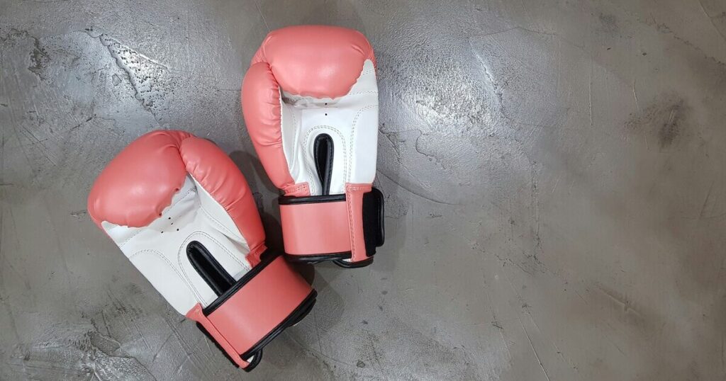 Red and white boxing gloves laid palms up on a cement floor.