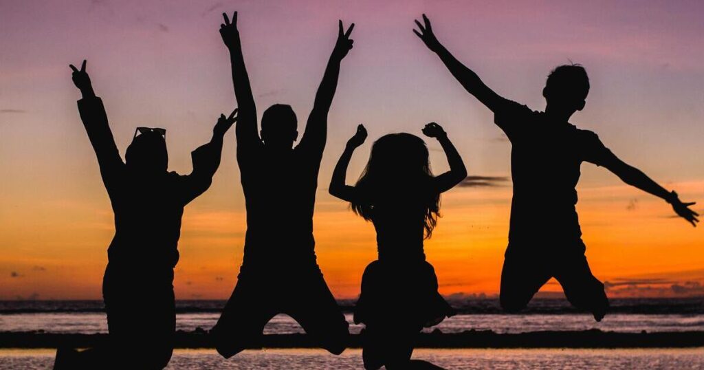Silhouette of four young adults jumping joyfully before an ocean sunset