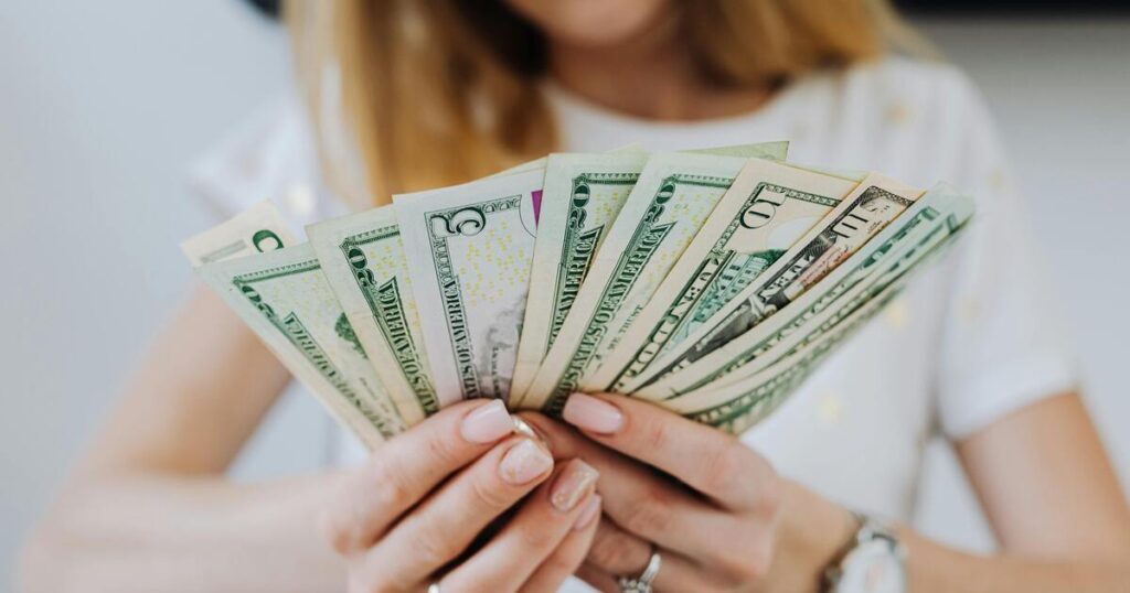 Woman holding a fan of U.S. dollar bills in both hands, with the cash spread out in front of her.